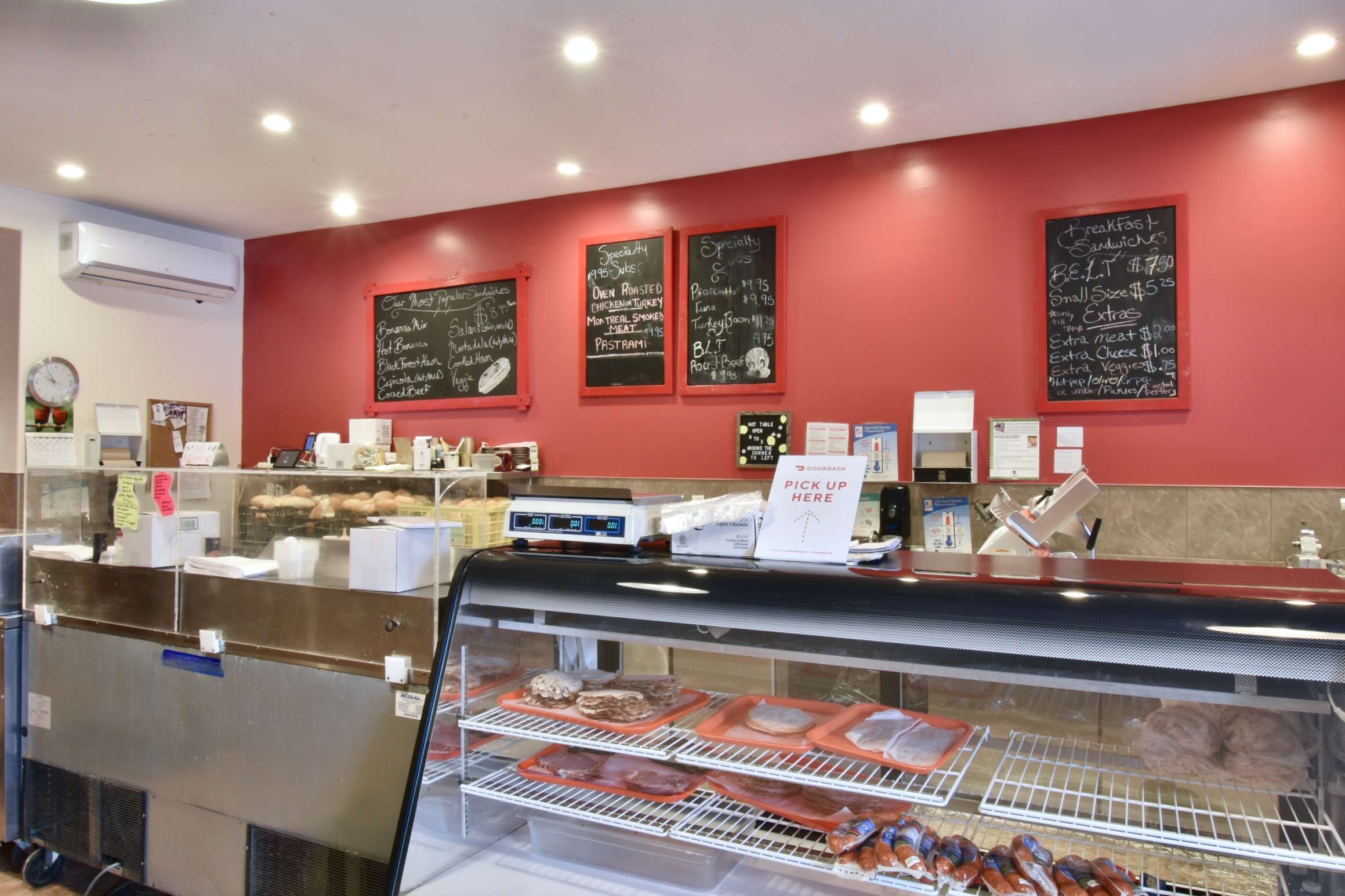 Wide view of Bonanza's deli meat counter, with handwritten menus in chalk posted on the walls. Pastries and deli meat are shown behind the front glass counter.