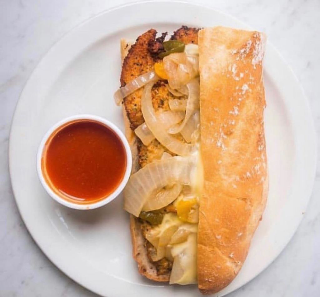 A chicken cutlet sandwich with sauce on the side on a plate.