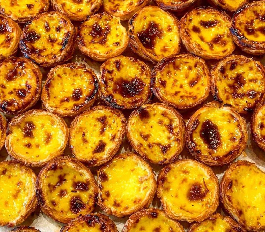 Many Portuguese egg custard tarts laid out in a honeycomb pattern on a baking tray.