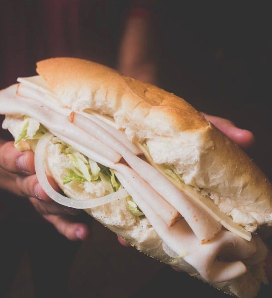 A person holding a turkey, onion, and lettuce submarine sandwich.