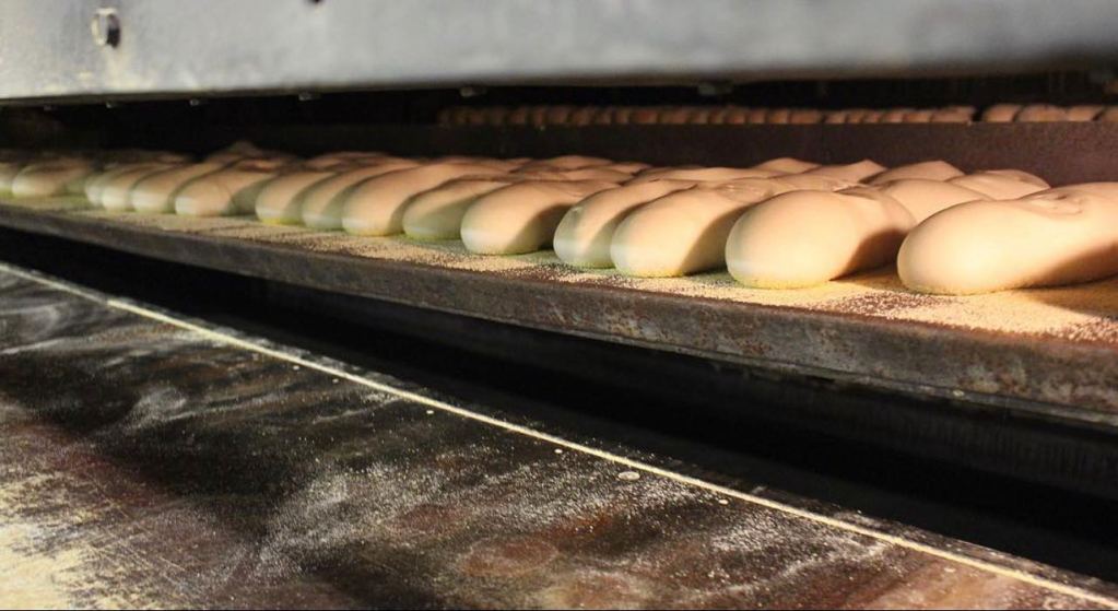 A row of bread-shaped dough inside an industrial oven, ready to be baked.